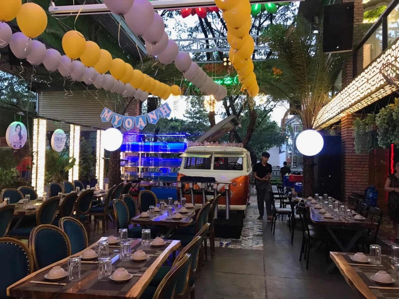 Khu ăn uống ngoài trời của Chóe Food Garden, Biên Hòa: bàn đã bày sẵn, xe VW cải tạo thành quầy bar và loa đen treo dưới mái bên phải.