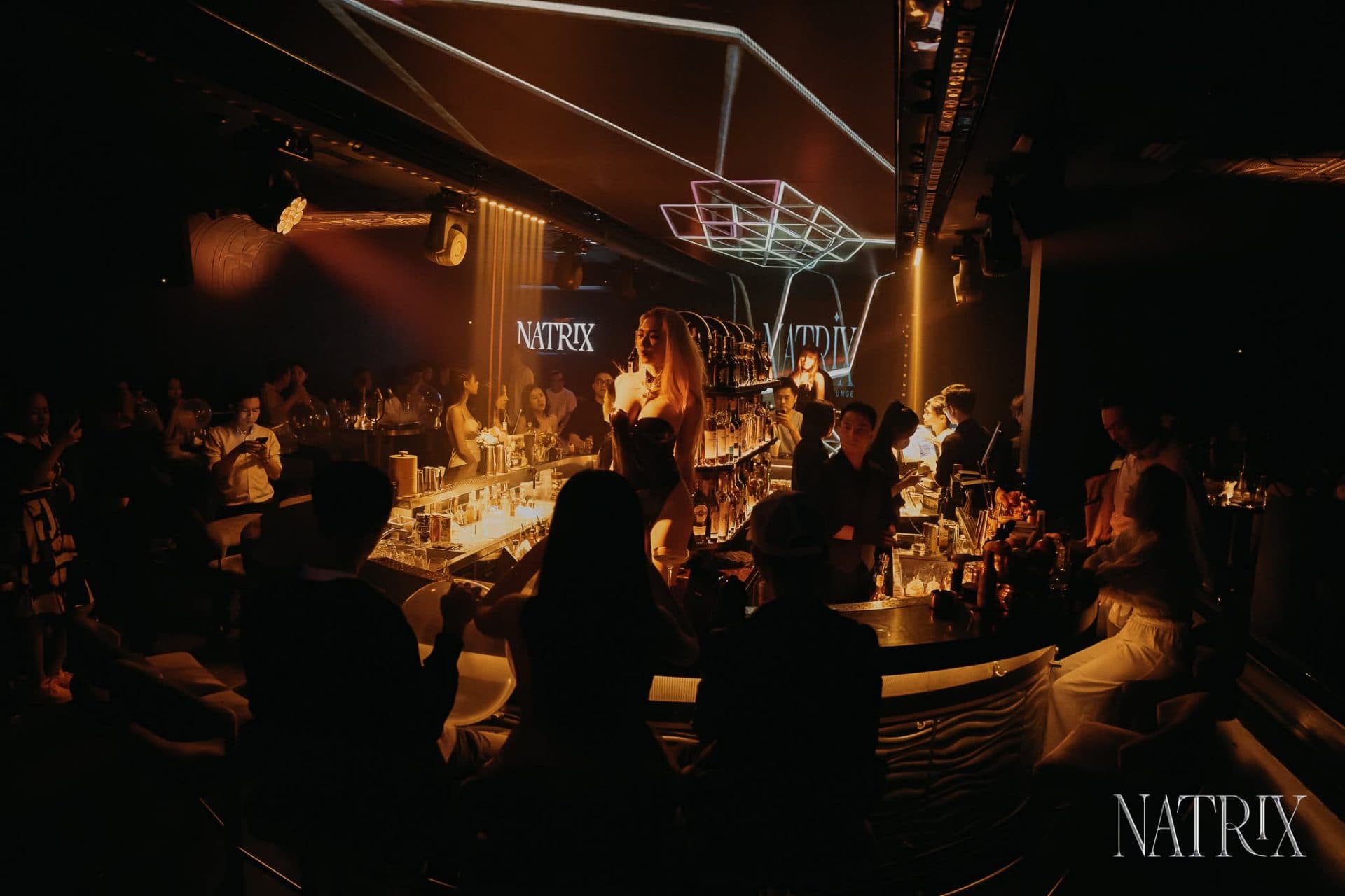 Không gian quầy bar Natrix về đêm với vũ công trình diễn và khách vây quanh quầy.