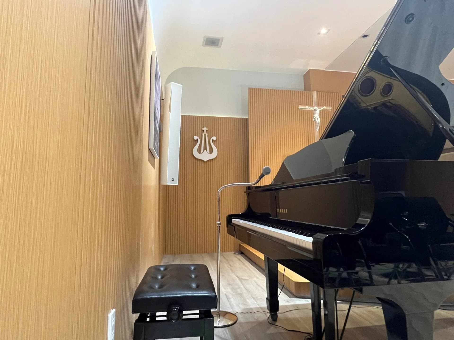 Micro Shure Beta 87A đặt trước đàn dương cầm, bên cạnh loa YME Luna gắn tường và tượng Thánh Giá tại Giáo Xứ Võ Dõng.