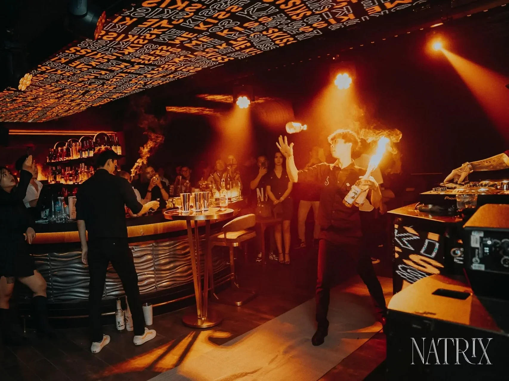 Nhân viên biểu diễn lửa (Flair Bartending) tại quầy bar trung tâm Natrix, không gian đông khách về đêm.