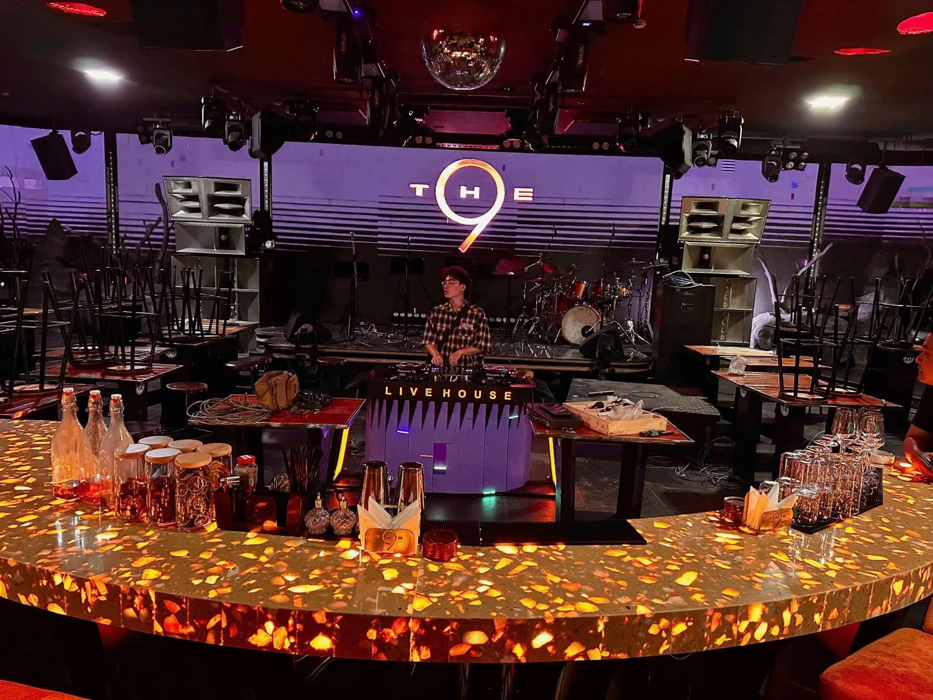 Sân khấu và quầy bar trung tâm tại The 9, với biển hiệu thương hiệu THE9 và bục DJ LIVE HOUSE, sau khi hoàn tất thi công.