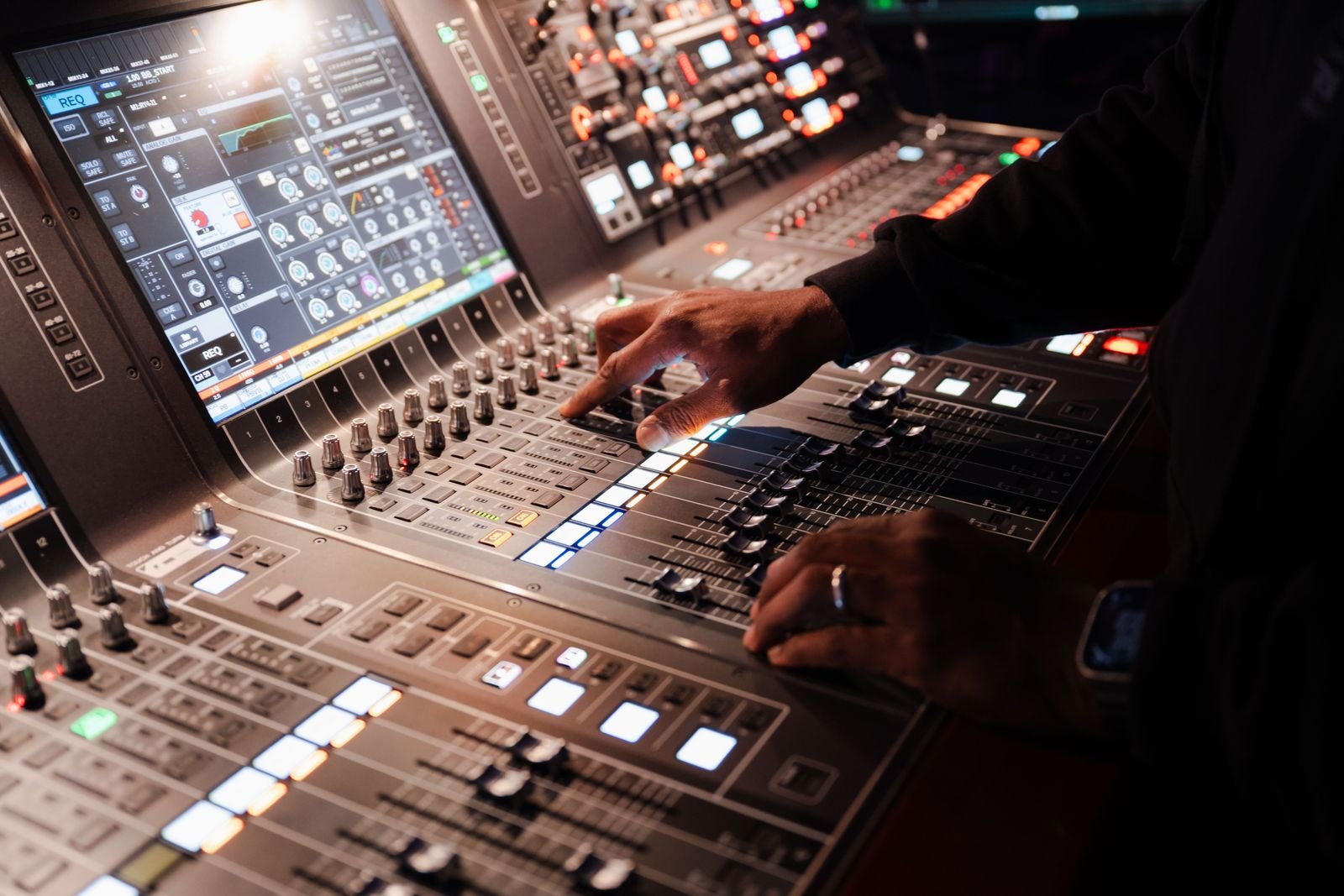 Tay kỹ sư điều chỉnh fader và channel strip trên mixer kỹ thuật số, màn hình hiển thị gain và EQ của kênh đang chọn.